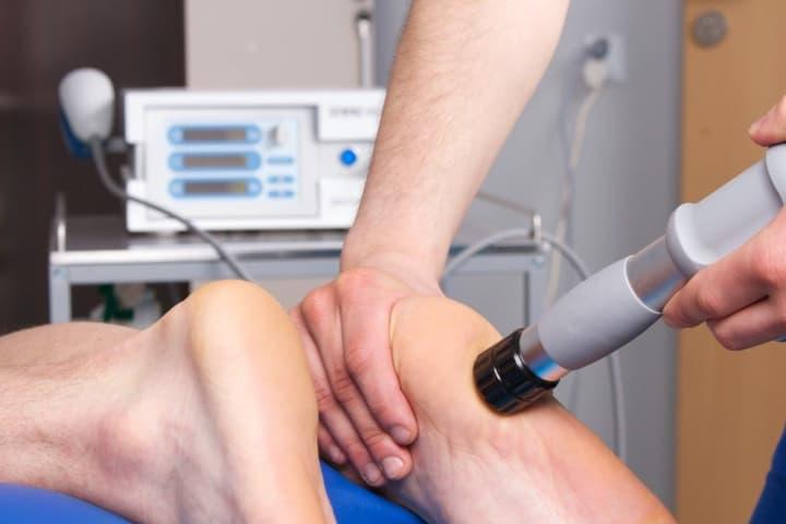 fizjoterapeuta wykonujący zabieg fali uderzeniowej na stopach pacjenta